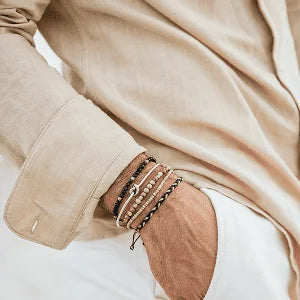 Stacked bracelets worn on a man’s wrist with a light linen shirt