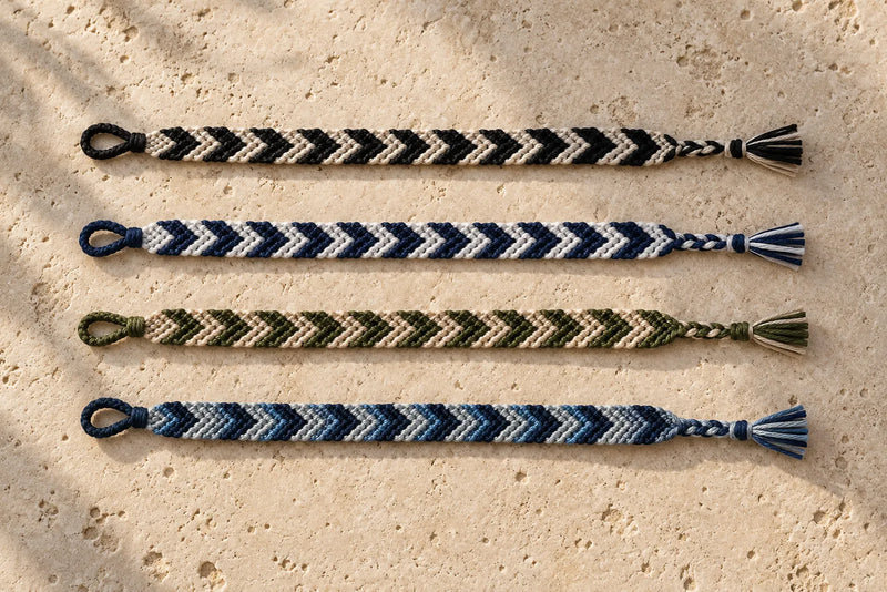 Four chevron friendship bracelets in black, navy, olive, and blue color combinations on travertine.