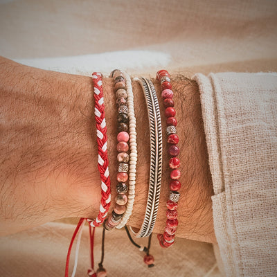 Handmade friendship bracelet in red and white stacked with bead and metal bracelets on wrist