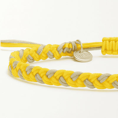 Close-up of friendship bracelet thread in yellow and gray with braided cord and charm
