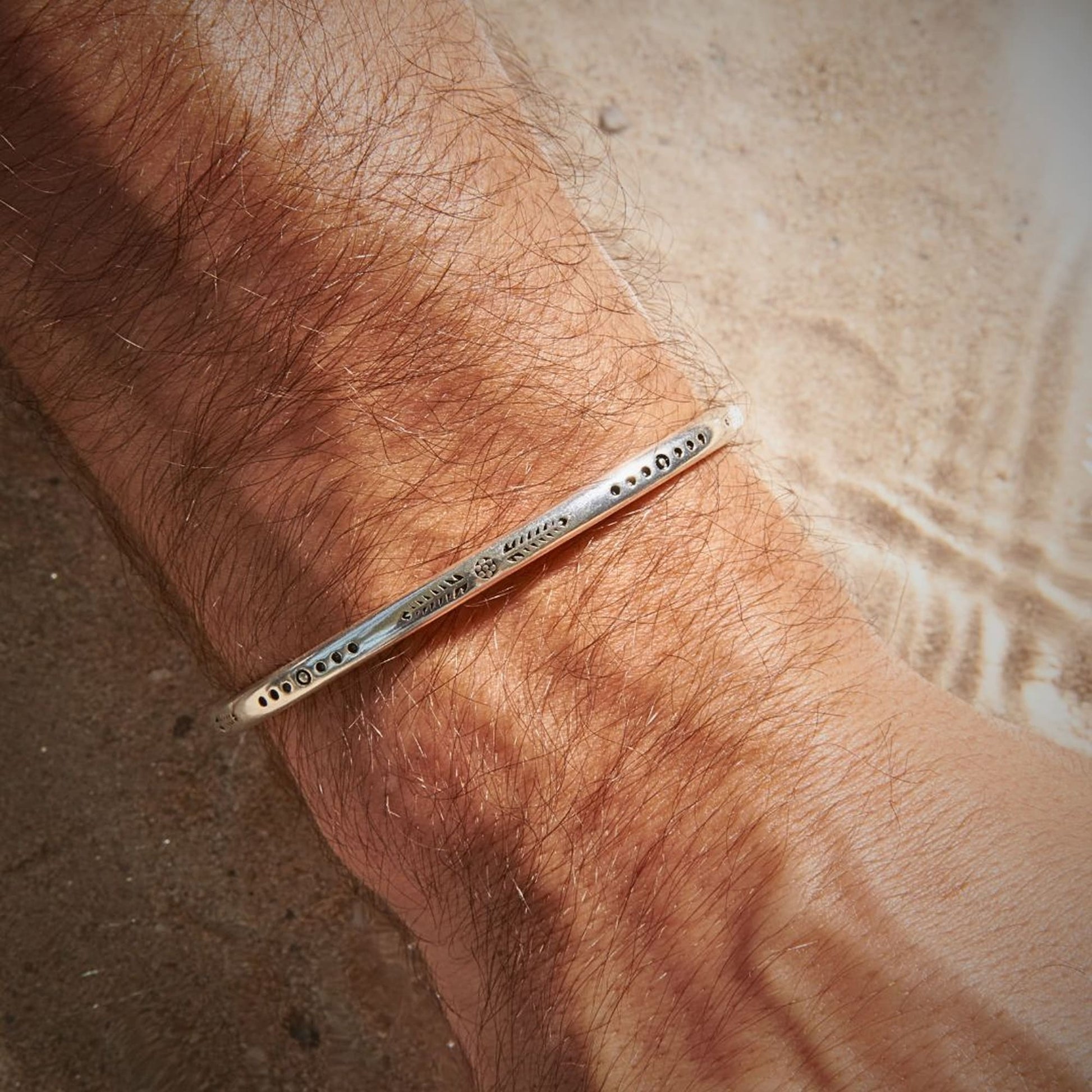 Slim silver cuff bracelet with unique engravings on man’s wrist at the beach.