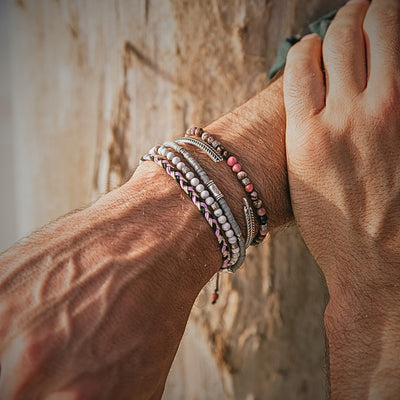 Close-up of Mallorca bracelet set worn on wrist, featuring pink, grey, and white beads with silver accents in a coastal setting