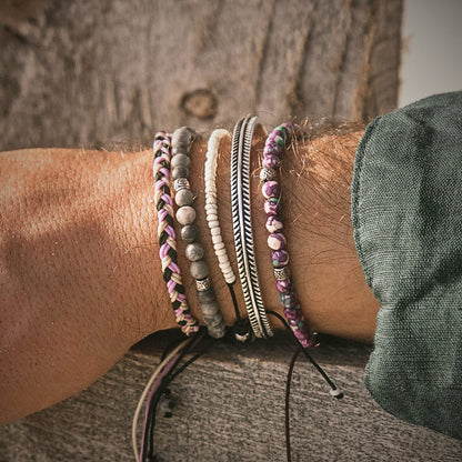 Wrist stacked with braided, beaded, and gray jasper bracelets in natural sunlight.