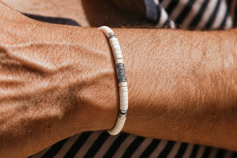 Men's white beaded bracelet close up with small white beads and a silver floral accent