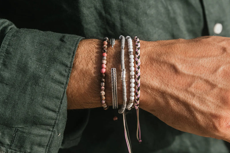 Men's white beaded bracelet stacked with colorful beads, silver cuffs, and woven bracelets
