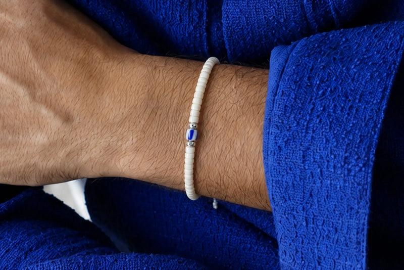 Men's white beaded bracelet with a blue accent bead worn against a bright blue outfit