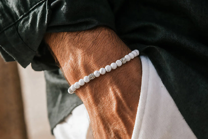 Men's white beaded bracelet with silver accents worn with a black jacket and white pants