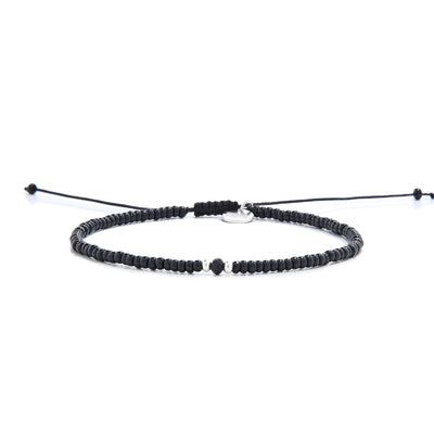 A mens beaded bracelet with glossy black beads, a faceted onyx bead, and a silver charm.