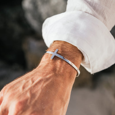 Stylish cross bracelet in silver, worn with casual white shirt.