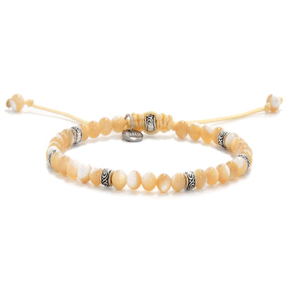 Close-up view of a mother of pearl bracelet with creamy yellow and white beads, featuring metal spacers and an adjustable yellow cord