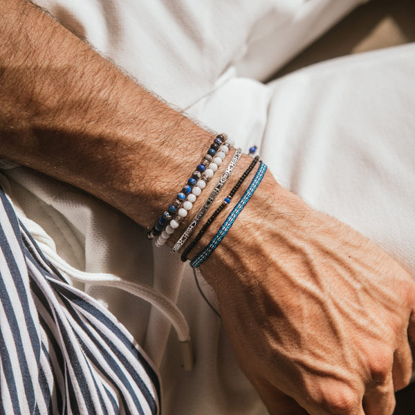 Stack of blue, black, and white beaded bracelets with silver accents on wrist.
