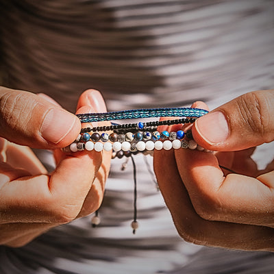 Hand holding a layered set of blue, black, and white bracelets in sunlight.