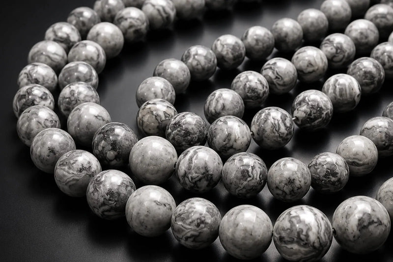 Natural gray gemstone beads with glossy marbled patterns arranged in strands against a dark background.