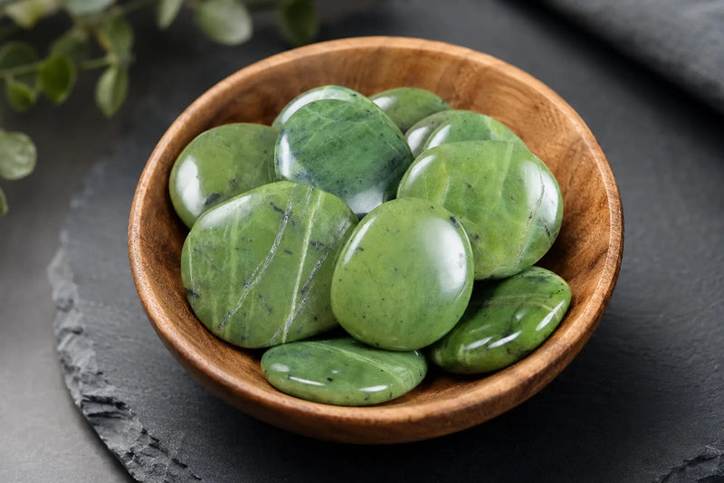 Jadeite vs Nephrite guide showing smooth light green nephrite stones arranged inside a wooden bowl.