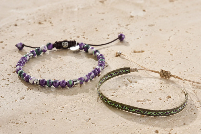 Purple and green bracelet color combo featuring a beaded bracelet and slim woven bracelet on light travertine