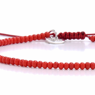 A top-down view of a round men beaded bracelet featuring small red beads and a silver charm on a white background.