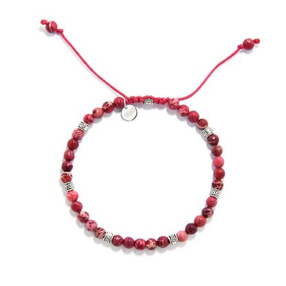 Red stone bracelet top view with round red beads, silver spacers, red cord, and charm.