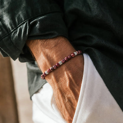 Red stone bracelet worn on a wrist with a dark green sleeve, white shirt, and silver spacers.