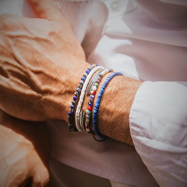 Person seated in a relaxed pose, showing a full view of the Santorini bracelet set styled with a white shirt.