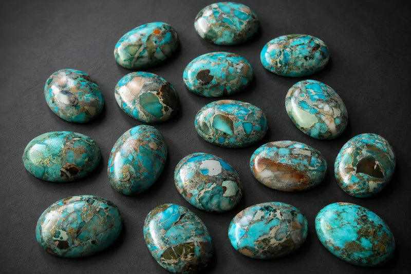 Sea Sediment Jasper polished oval cabochons in turquoise, cream, brown and grey tones on a dark background.