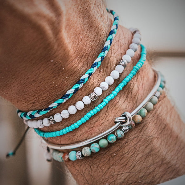 Close-up of a wrist wearing the Sicily beaded bracelet set with white, turquoise, and braided blue cords.