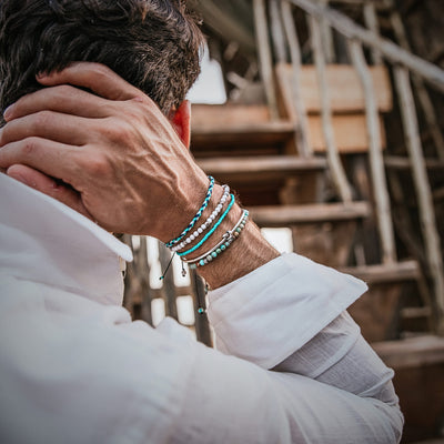 Man in a white shirt wearing the full Sicily bracelet set, viewed from behind near a rustic staircase.