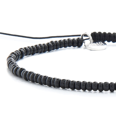 Angled side shot of black bead bracelet showing cord and charm