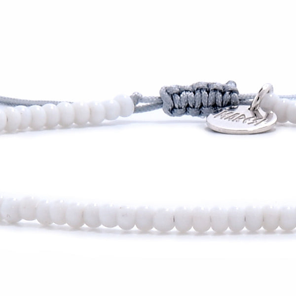Small beaded bracelets in white with gray cord and silver charm close-up