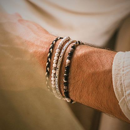 Close-up of neutral-toned stacked bracelet sets featuring beads and braided cord on a man's wrist.