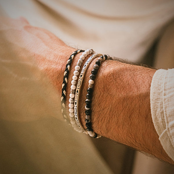 Close-up of neutral-toned stacked bracelet sets featuring beads and braided cord on a man's wrist.