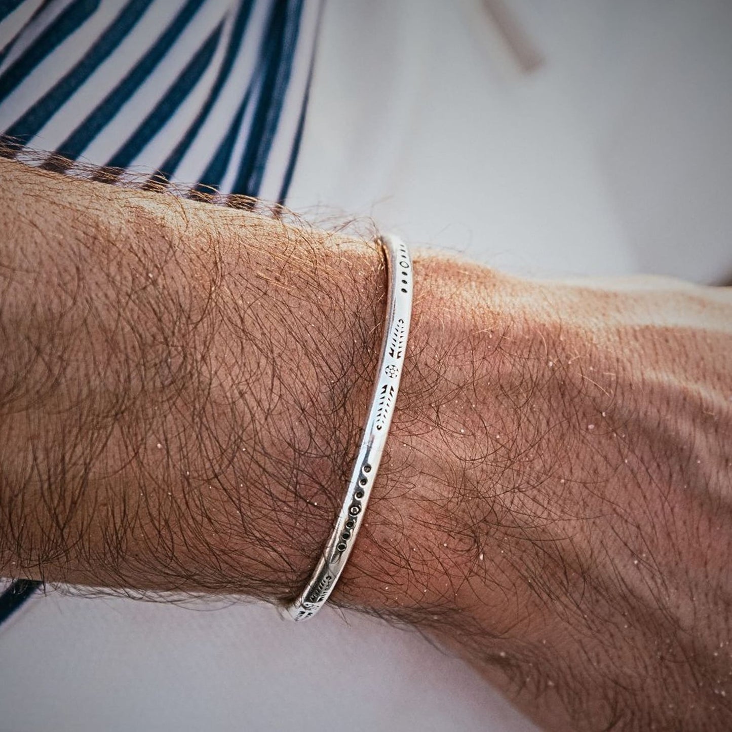Elegant silver cuff bracelet with engraved design worn on wrist.