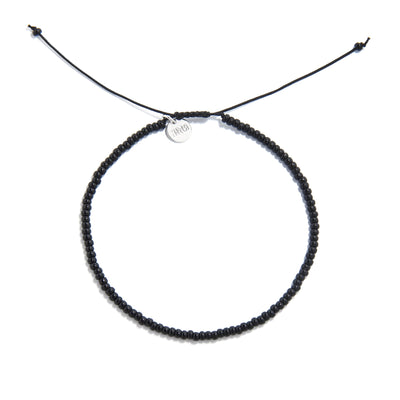 A top-down shot of a black bead bracelet forming a circle, showing a silver charm and adjustable cord ends.