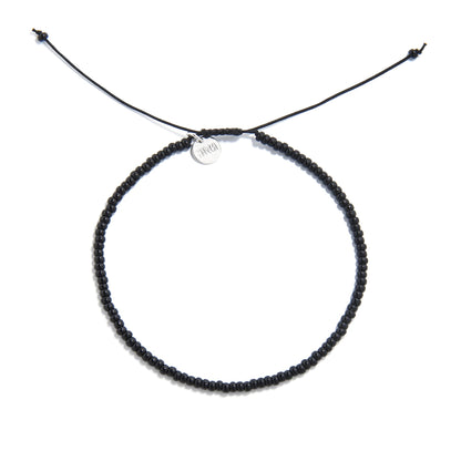 A top-down shot of a black bead bracelet forming a circle, showing a silver charm and adjustable cord ends.