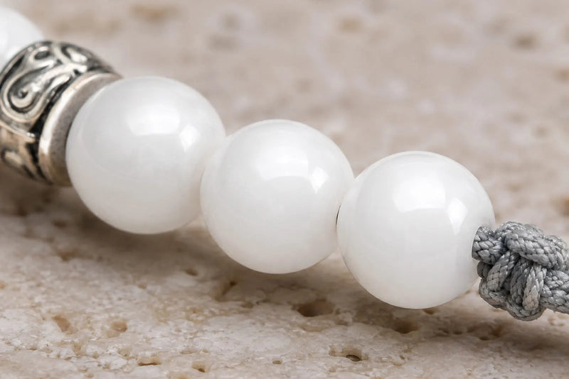 Macro view of polished white jade beads, silver detail and gray cord showing bead finish and bracelet construction