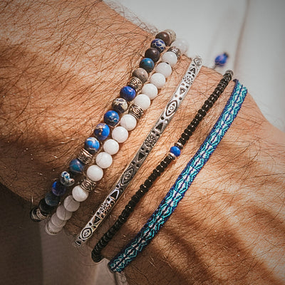 Stylish white jade stone bracelet stacked with blue and silver bracelets on a wrist.