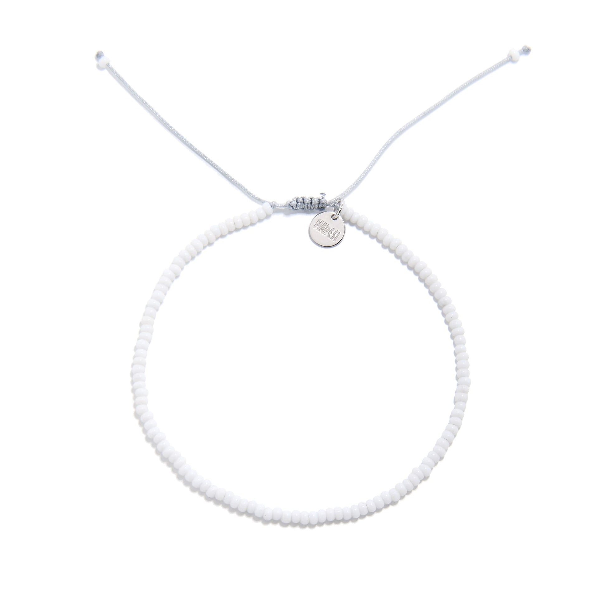 Overhead view of small beaded bracelet in white with fine seed beads and silver logo charm