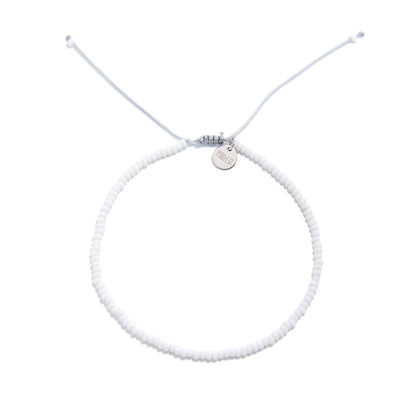 Overhead view of small beaded bracelet in white with fine seed beads and silver logo charm