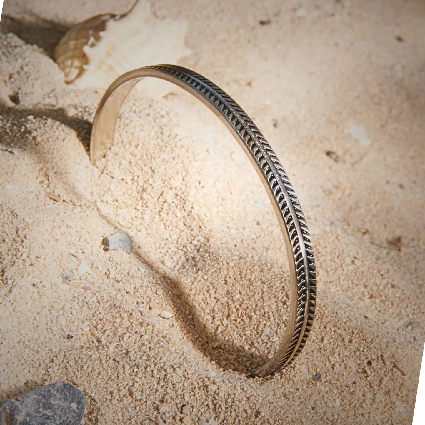 Bangles Bracelets displayed upright in sand, showing engraved feather pattern and open cuff shape