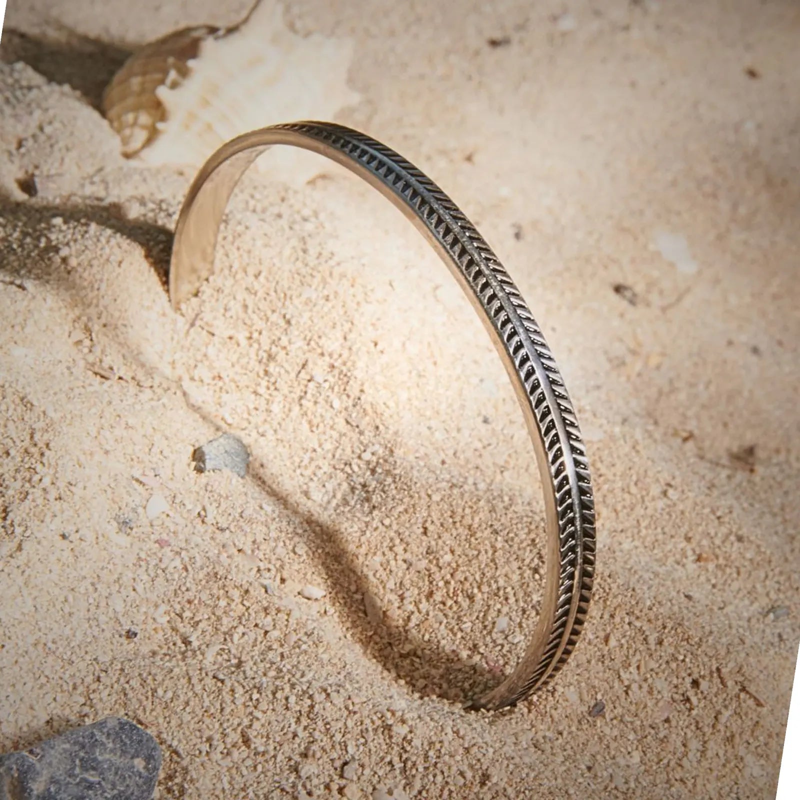 Bangles Bracelets displayed upright in sand, showing engraved feather pattern and open cuff shape