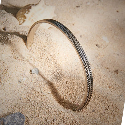 Bangles Bracelets displayed upright in sand, showing engraved feather pattern and open cuff shape