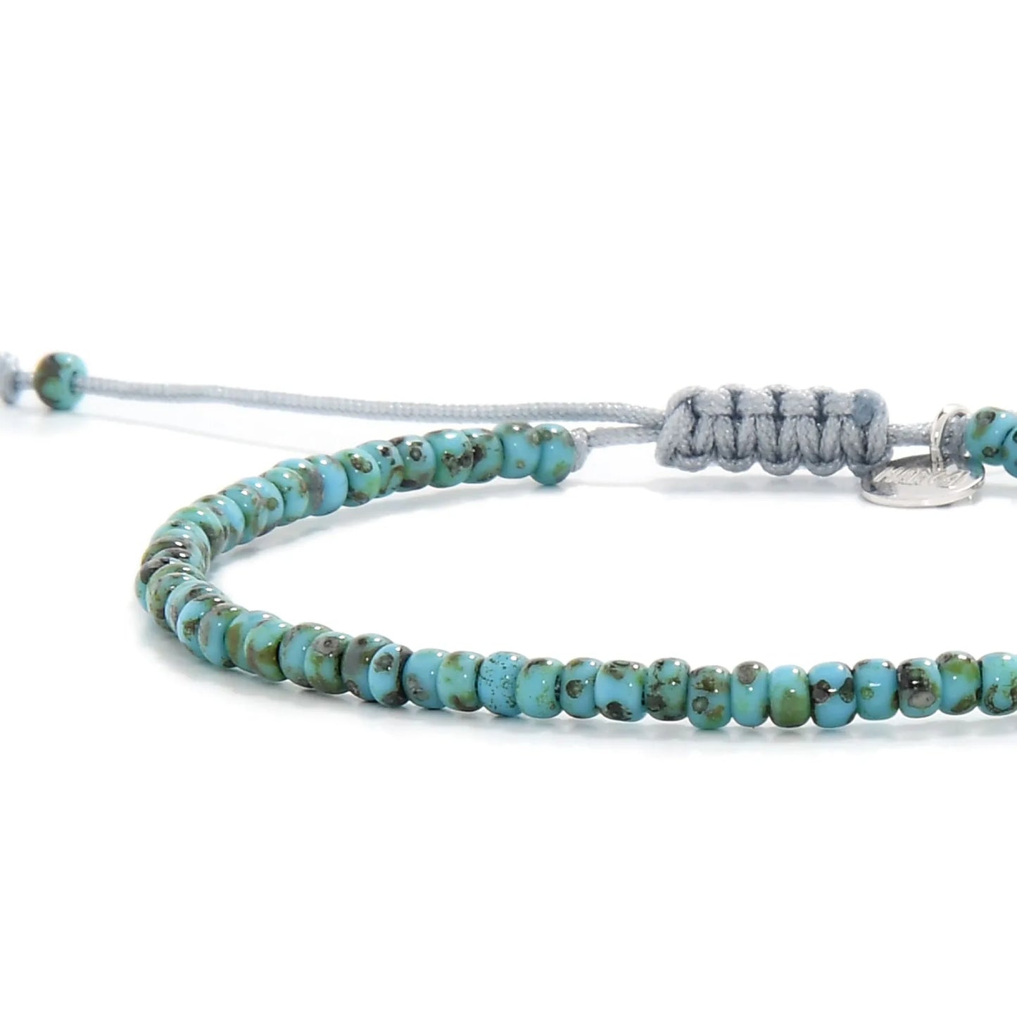 Close-up of Bead Bracelet showing turquoise Picasso seed beads with gray cord, silver charm, and cord closure