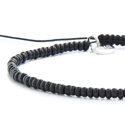 Detailed view of Black Bead Bracelet with black seed beads with silver charm, seed bead texture, and cord knot