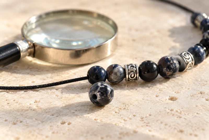 Black jasper bead illustration with a loose drilled bead, patterned bracelet and magnifying glass.