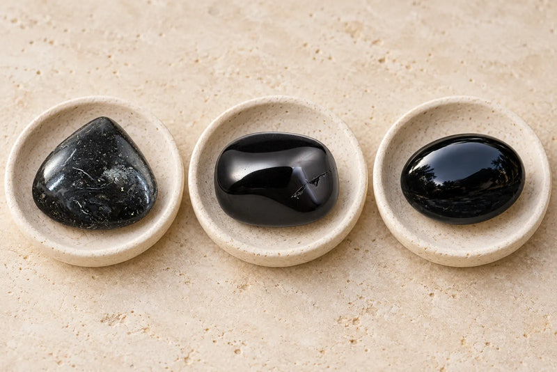 Black jasper comparison illustration with three polished dark stones displayed in pale stone dishes.
