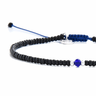 Close-up of black and blue bead bracelet showing black seed beads with blue accent beads, silver charm, and cord closure