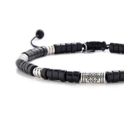 Close-up of black shamballa bracelet showing black clay beads with engraved silver spacers, silver charm, and cord closure