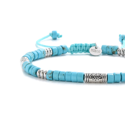 Close-up of Bracelet of Clay showing turquoise clay beads with engraved silver spacers, silver charm, and cord closure