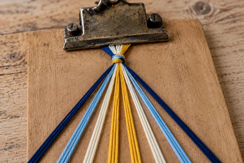 Chevron bracelet setup with navy, light blue, ivory, and yellow floss arranged in mirrored pairs on a clipboard.