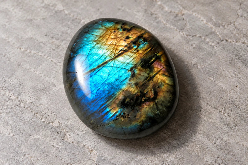 Dark labradorite cabochon showing blue, turquoise, and golden reflections