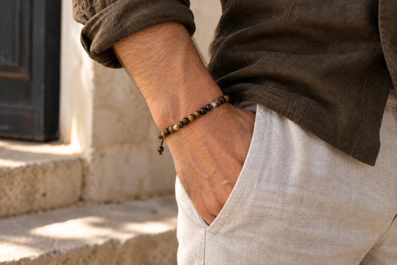 Man wearing a golden-brown and dark beaded bracelet with an olive shirt and light trousers